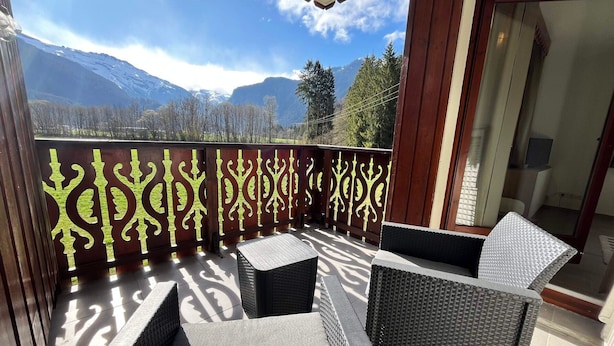 Un balcon agrémenté de meubles en osier et d’une grille décorative en métal, offrant une vue sur un paysage montagneux.