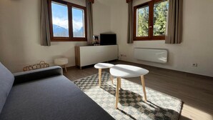 Un salon moderne avec un canapé, deux petites tables, un téléviseur et un radiateur.