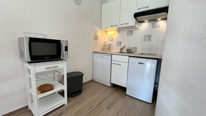 Une cuisine compacte avec des meubles blancs, un four à micro-ondes, un lave-vaisselle et une poubelle.