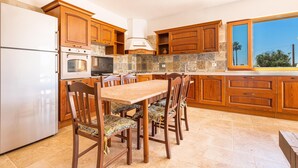 Een keuken met houten kastjes, een witte koelkast, een fornuis en een eettafel met stoelen.