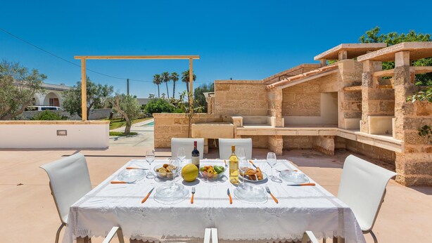 Een terras met een tafel voor twee personen, omgeven door stenen bouwwerken en een helderblauwe lucht.