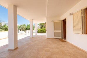 Un espace extérieur abrité, doté d’un sol carrelé, de murs blancs et d’une porte à volets.
