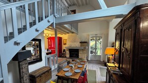 A dining area with a wooden table, chairs, and a fireplace. A staircase with a railing leads to an upper level. - Magnifique Villa de 14 Pers Piscine Chauffée, Jacuzzi, Sauna (Saint-Martin-des-Champs)
