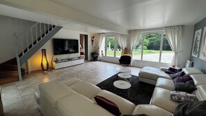A spacious living room with a large TV, a sofa, a coffee table, and a staircase. - Magnifique Villa de 14 Pers Piscine Chauffée, Jacuzzi, Sauna (Saint-Martin-des-Champs)