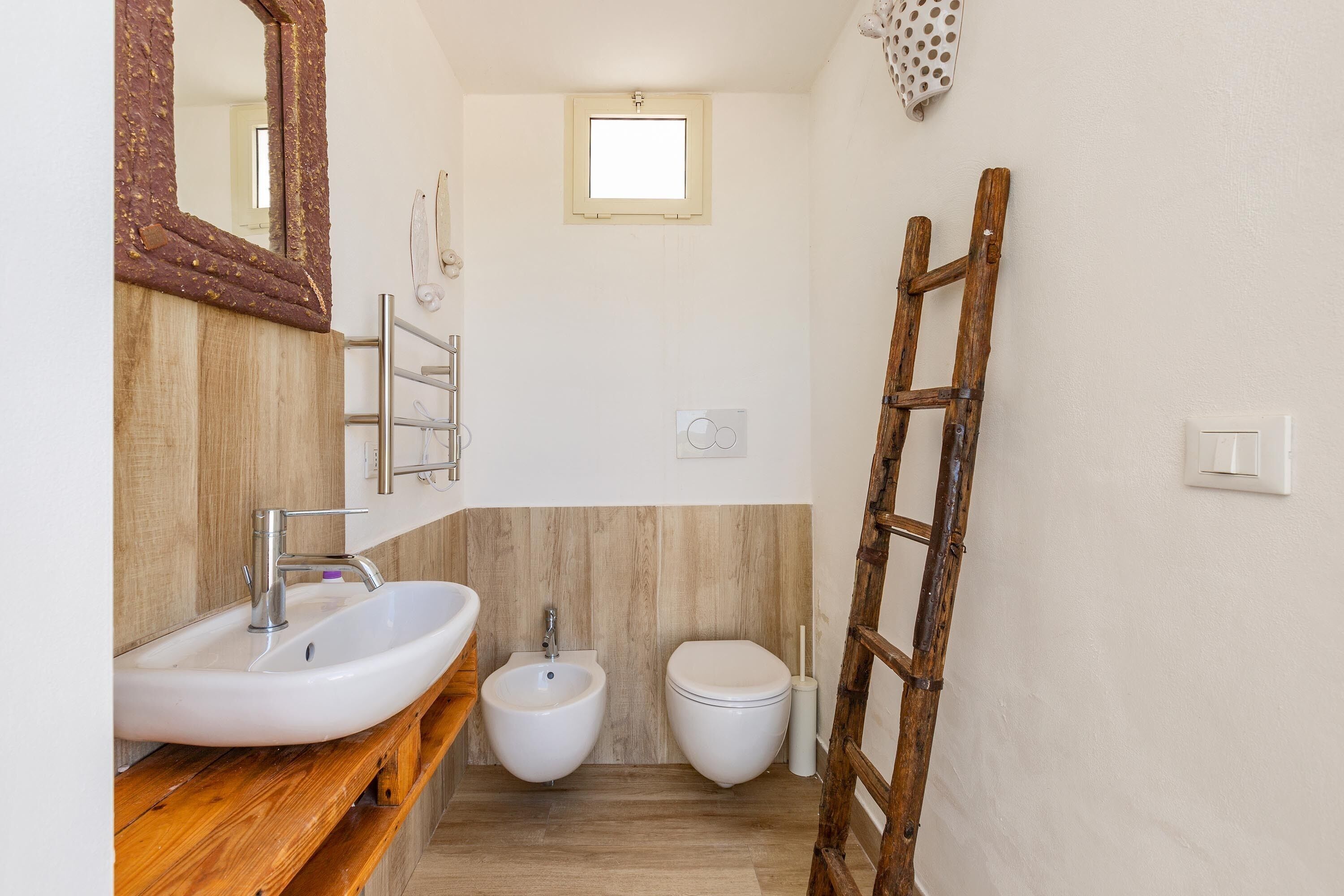 Un baño con tocador de madera, un lavamanos blanco, un bidé y un inodoro.