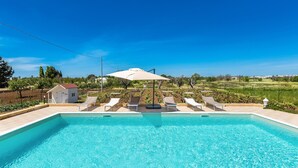 A rectangular swimming pool with clear blue water, surrounded by lounge chairs and umbrellas, set against a backdrop of a vineyard and clear sky. - 2340 Villa Il Neto by Perle di Puglia (Casarano)