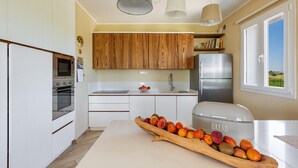 A modern kitchen with white cabinets, wooden upper cabinets, stainless steel appliances, and a fruit bowl on the counter. - 2340 Villa Il Neto by Perle di Puglia (Casarano)