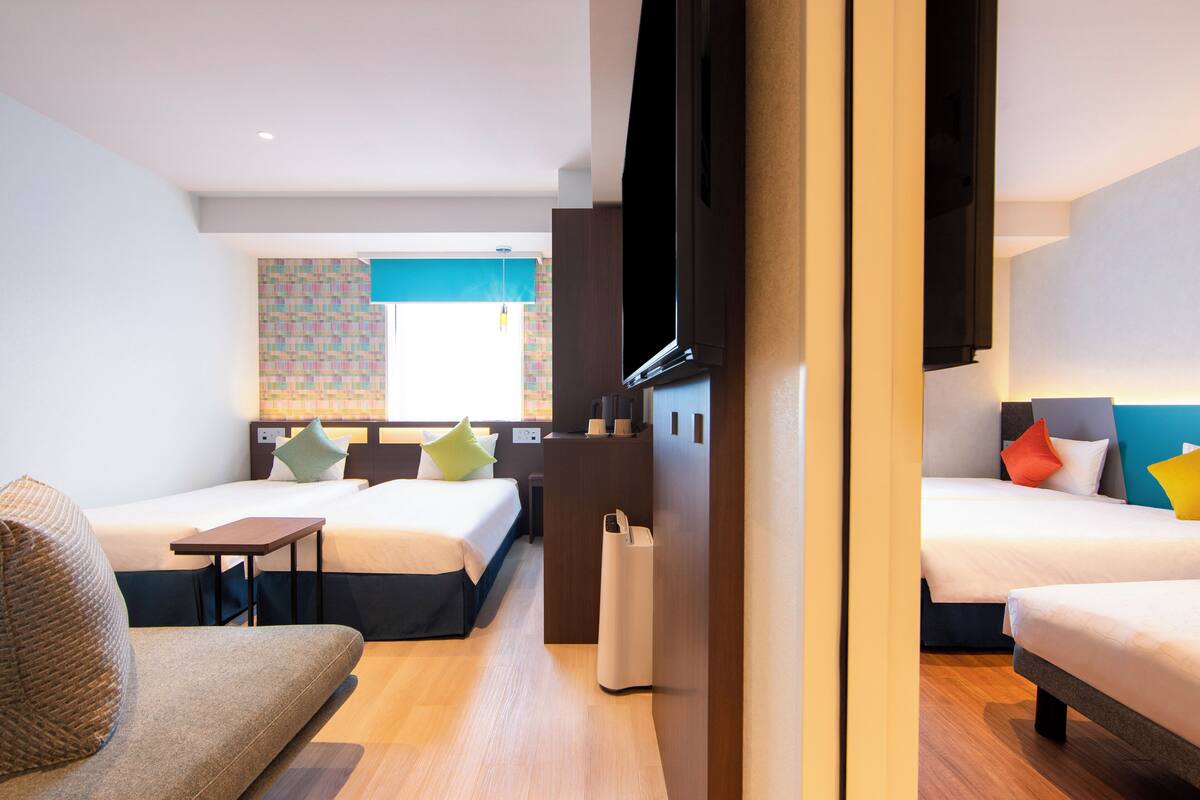 A hotel room with two beds, a sofa, a desk, and a TV.