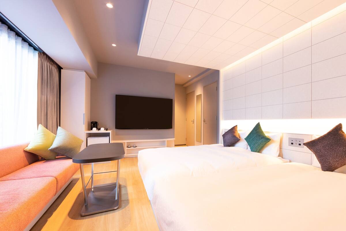 A modern hotel room with a large bed, a sofa, a flat-screen TV, and a small table.