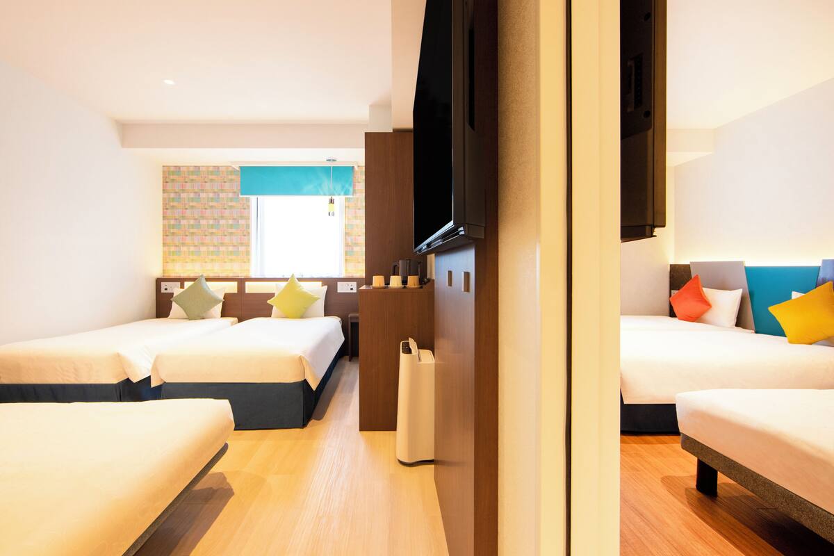 A hotel room with two beds, a TV, and a window with a view of a building.