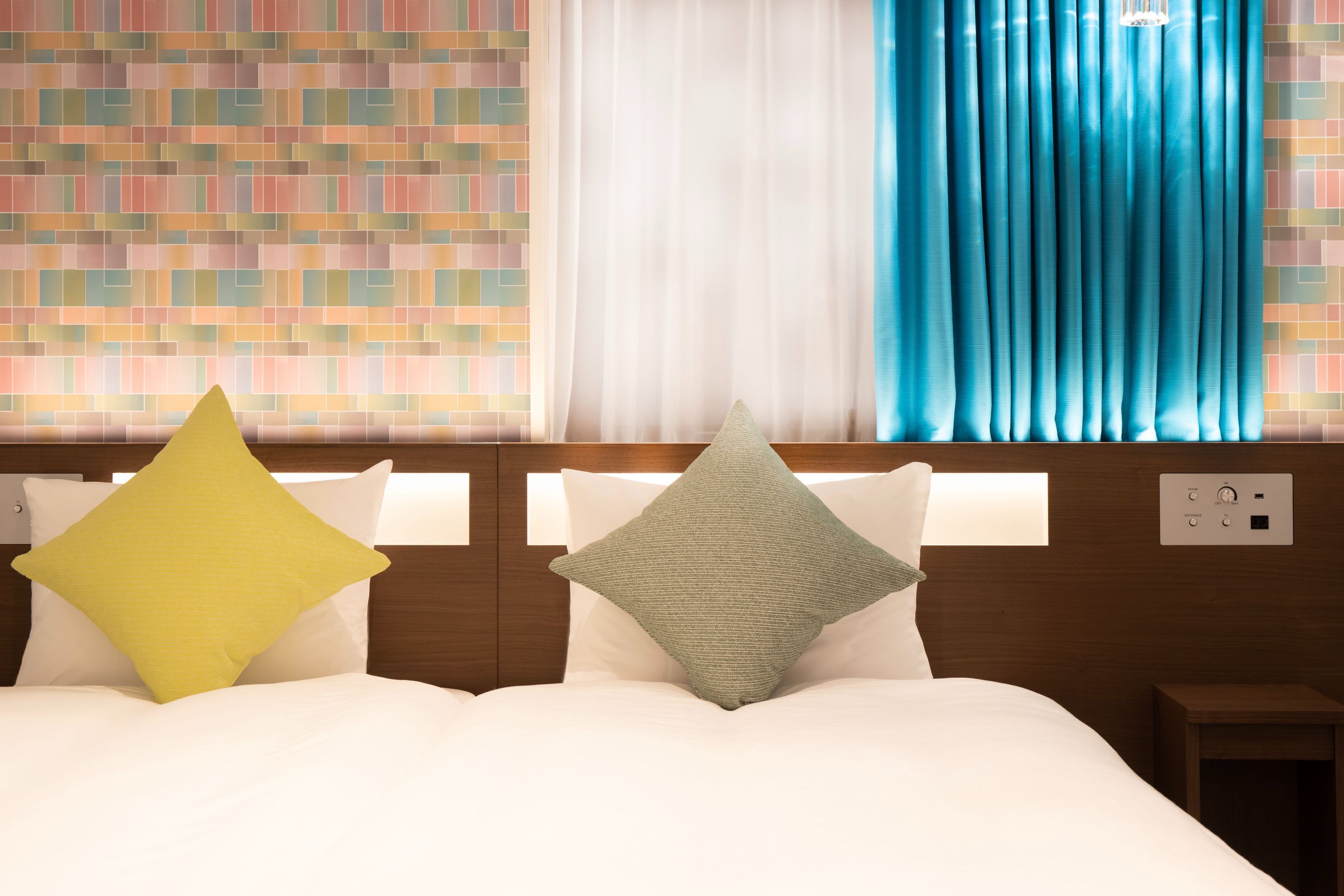 Une chambre d’hôtel avec un lit bien fait, un mur décoré d’un motif et une fenêtre avec des rideaux.