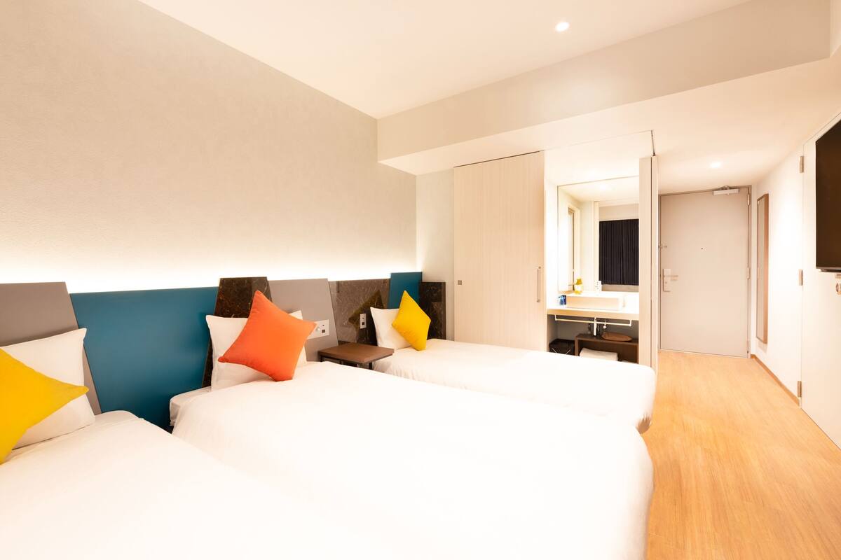 A hotel room with two beds, a bedside table, a mirror, and a door leading to another room.