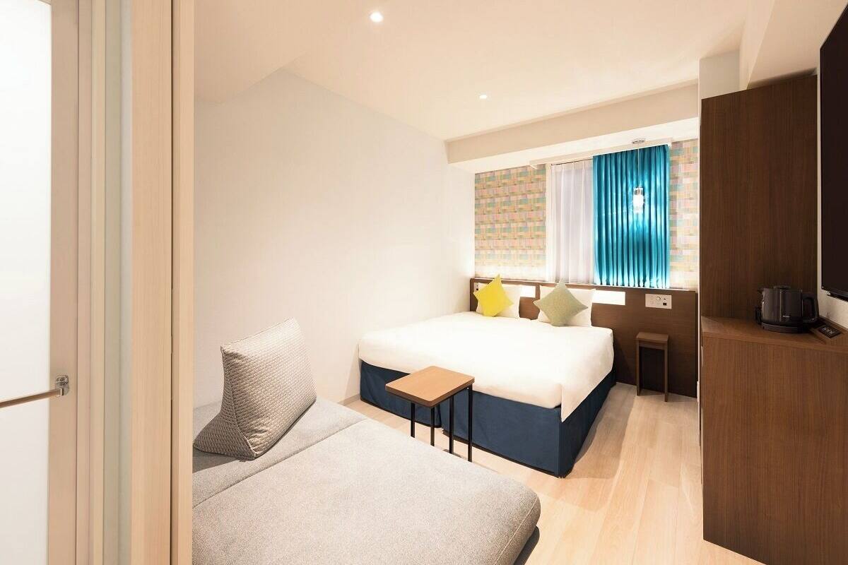 A hotel room with a bed, a sofa, a small table, a TV, and a coffee maker.