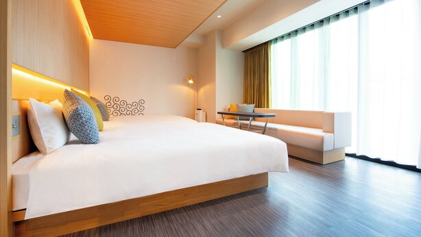 A modern hotel room with a large bed, a small table, a sofa, and a large window with curtains. - Karaksa Hotel Colors Tokyo Yaesu (Tokyo)