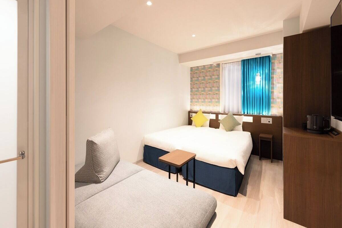 A hotel room with a bed, a sofa, a small table, a TV, and a window with curtains.
