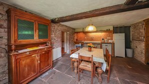 Een landelijke keuken met stenen muren, houten kastjes, een eettafel met stoelen en een hanglamp.