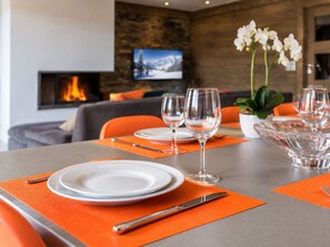 A dining table set with plates, cutlery, and wine glasses, with a fireplace and a television in the background.