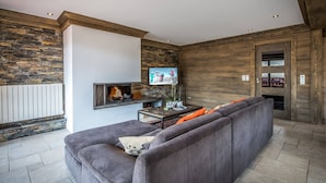 Ein modernes Wohnzimmer mit einer Steinwand, einem Kamin, einem Fernseher und einem Sofa mit orangefarbenen Kissen.