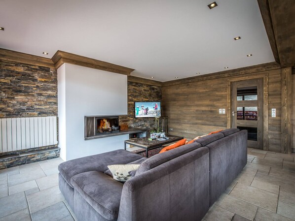 A modern living room with a stone wall, a fireplace, a television, and a sofa with orange cushions.