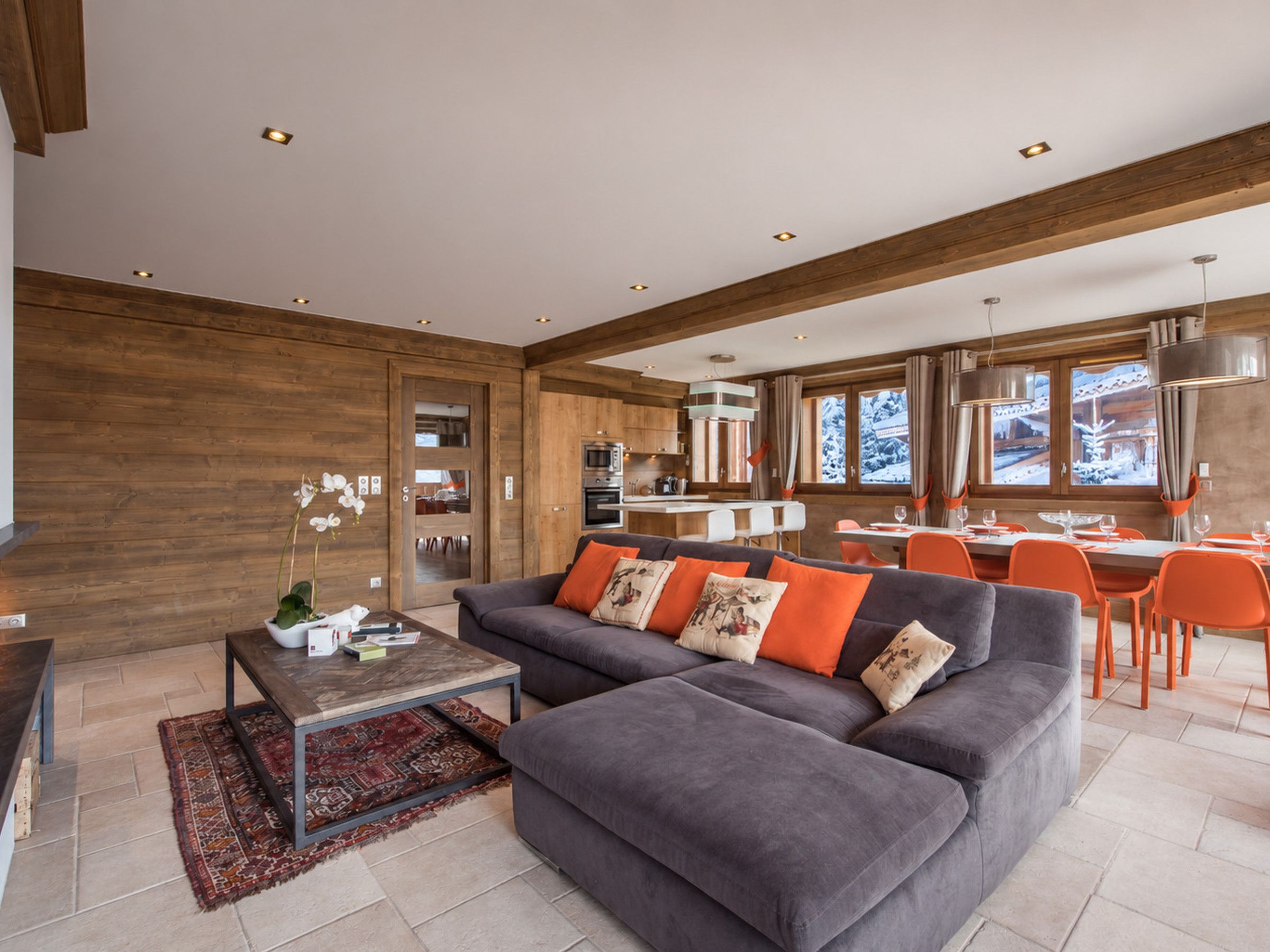A modern living room with a sectional sofa, a coffee table, and a dining area with orange chairs.