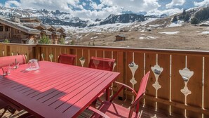 Ein roter Tisch und Stühle auf einem Balkon mit Blick auf schneebedeckte Berge und Holzhäuser.