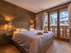 Une chambre à coucher aux murs lambrissés, avec un lit, deux tables de chevet et une fenêtre donnant sur un paysage enneigé.