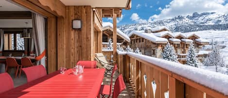 A wooden deck with a red table and chairs, overlooking a snowy mountain landscape.