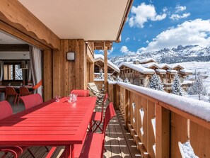 A wooden deck with a red table and chairs, overlooking a snowy mountain landscape.