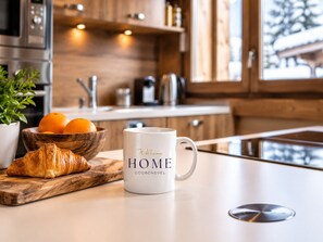 A kitchen counter with a white mug, a wooden bowl with oranges, and a croissant.