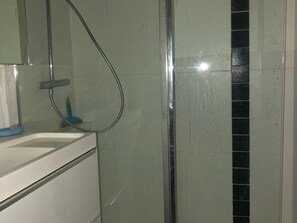 Un baño con cabina de ducha de vidrio, un lavabo blanco y un espejo.