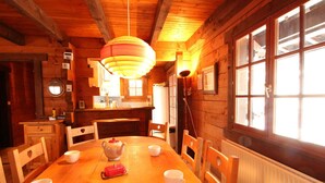 Une salle à manger en bois avec une grande table, des chaises, une bouilloire rouge et une lampe suspendue.