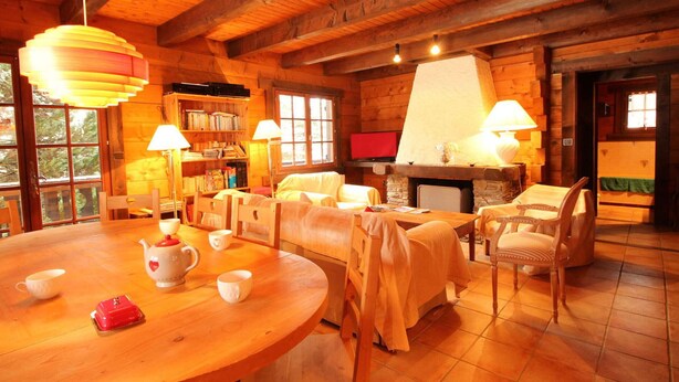 L’intérieur d’un chalet confortable, avec des murs en rondins, une table à manger en bois, des chaises, une cheminée et une bibliothèque.