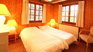 Une chambre dans une cabane en bois, avec deux lits, une chaise et une fenêtre avec des rideaux.