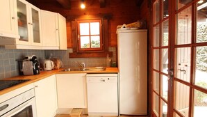 Une cuisine compacte avec des meubles blancs, un lave-vaisselle, une cuisinière et une fenêtre donnant sur un espace verdoyant.