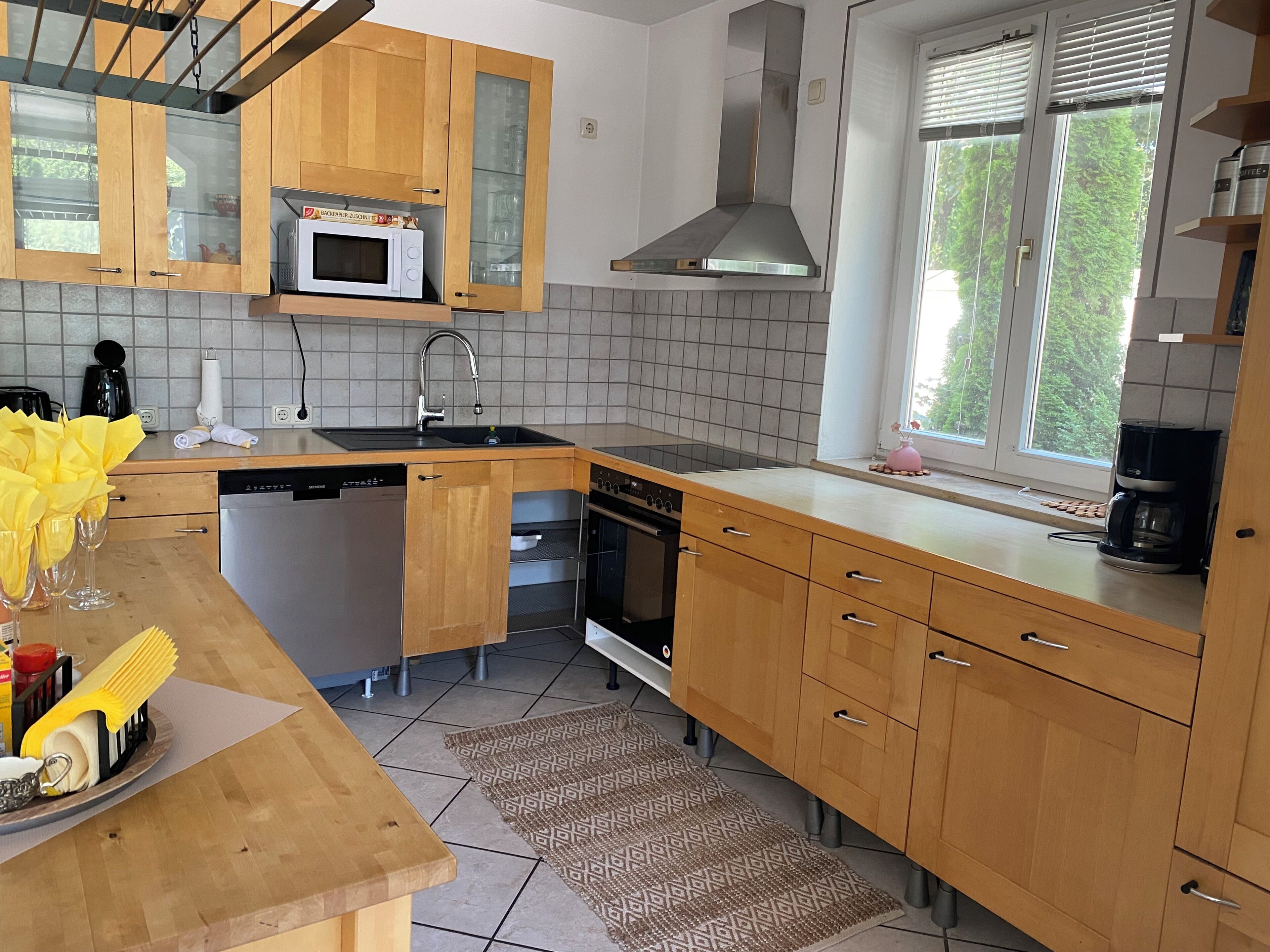 Eine moderne Küche mit Holzschränken, einer Mikrowelle, einem Geschirrspüler, einem Backofen und einem Fenster mit Jalousien.