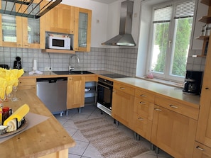 Une cuisine moderne avec des meubles en bois, un four à micro-ondes, un lave-vaisselle, un four et une fenêtre avec des stores.
