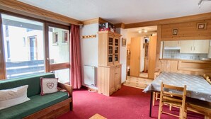 Une pièce chaleureuse avec un canapé vert, une table en bois et un coin cuisine doté de meubles en bois et d’une fenêtre.