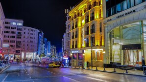Una calle iluminada en la ciudad de noche, con edificios, incluyendo un hotel con un letrero que dice "DIANA KLIK TEKSTIL".
