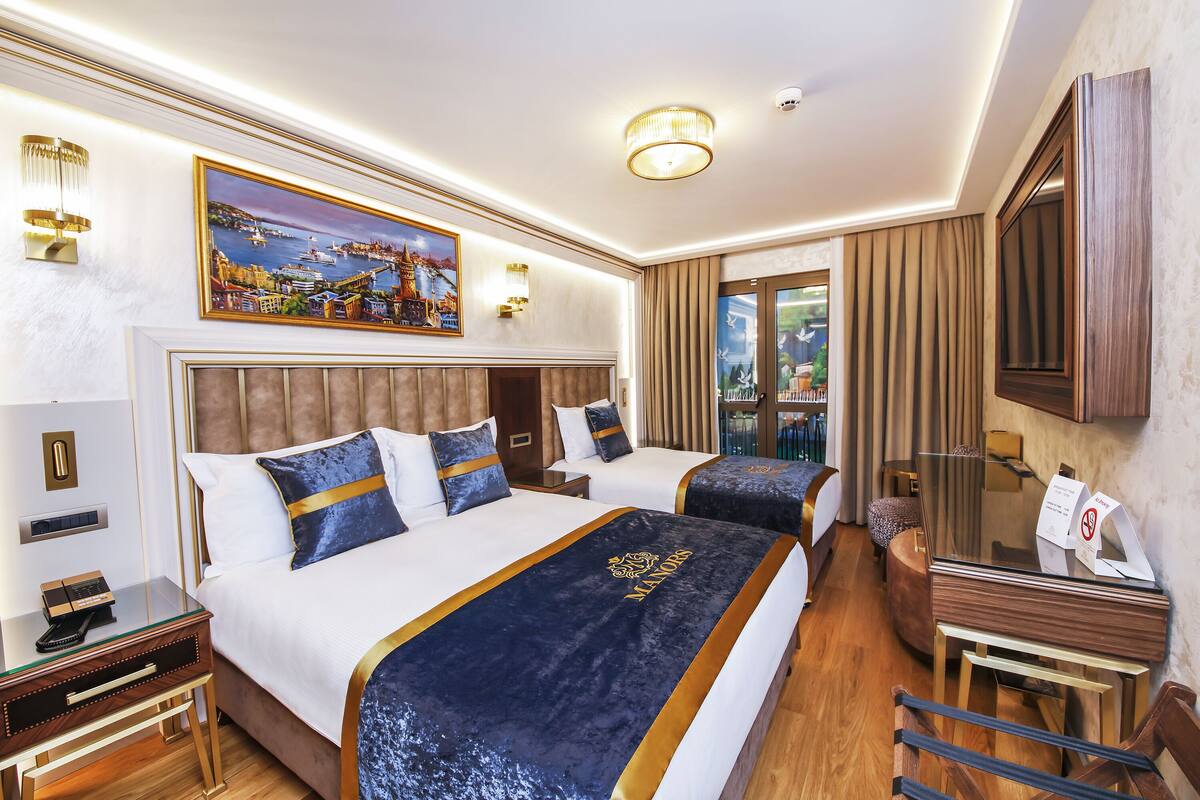 A hotel room with two beds, a large painting, a desk with a telephone, and a view of the outdoors.