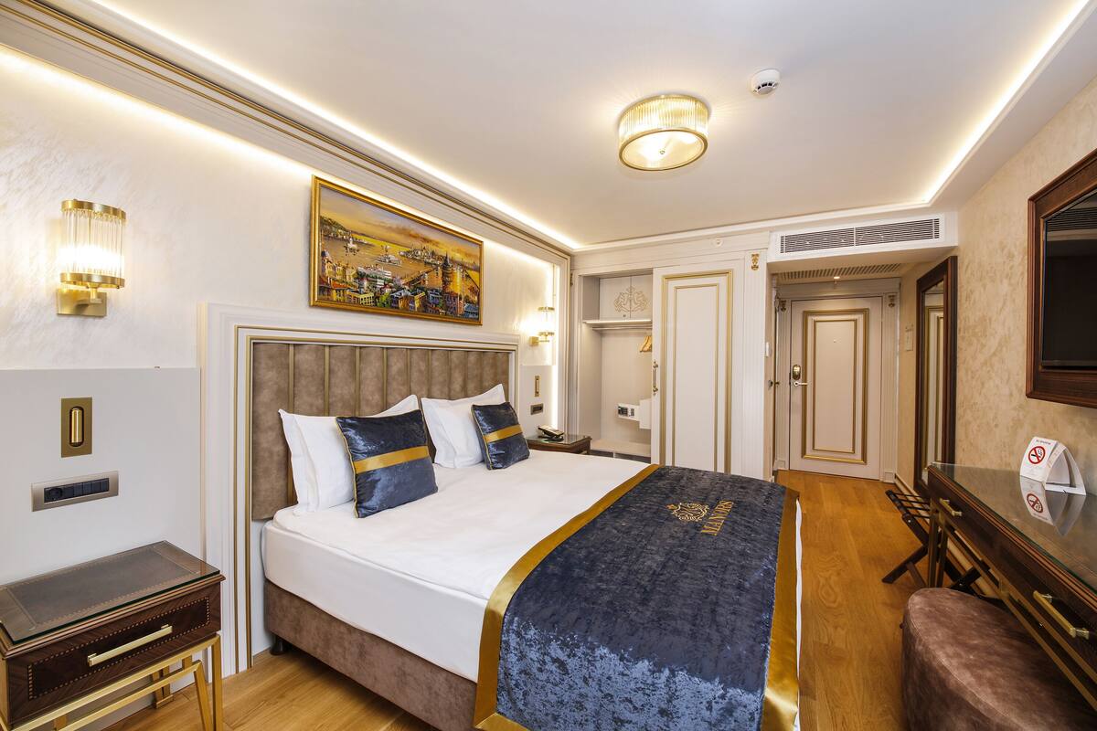 A hotel room with a large bed, a bedside table, a mirror, and a painting on the wall.