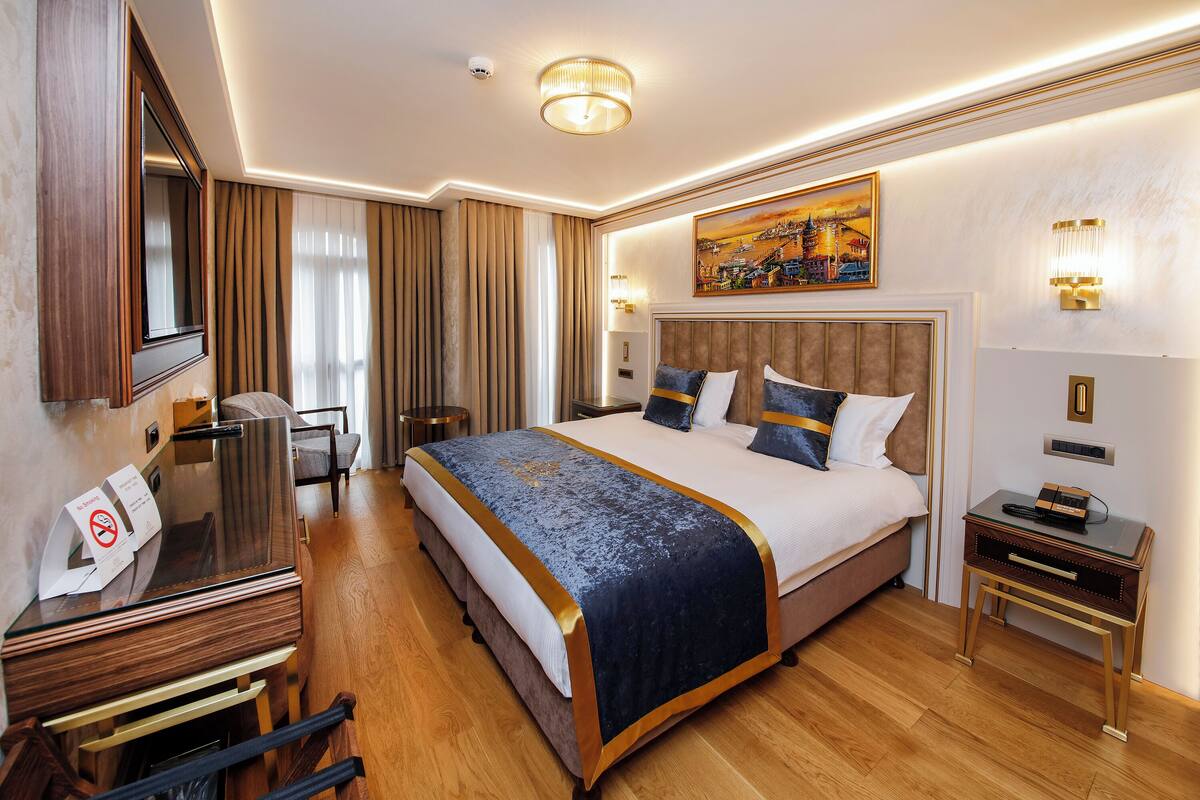 A hotel room with a large bed, a desk, a chair, a nightstand, and a painting on the wall.