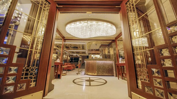 Un lobby de hotel lujoso con una gran araña, puertas de madera ornamentadas y un suelo pulido.