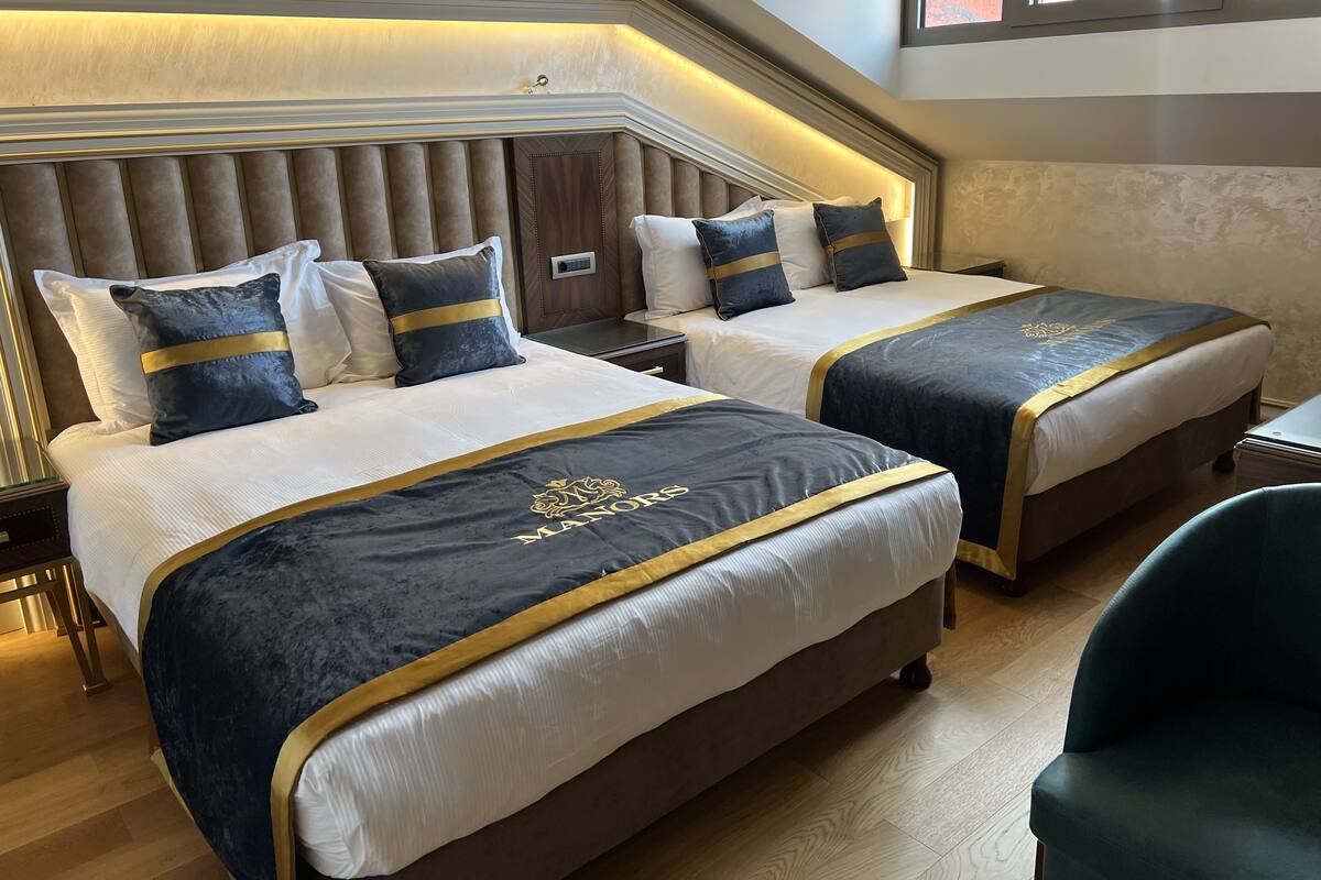 A hotel room with two beds, each with a dark blue bedspread and gold trim, and a large padded headboard.