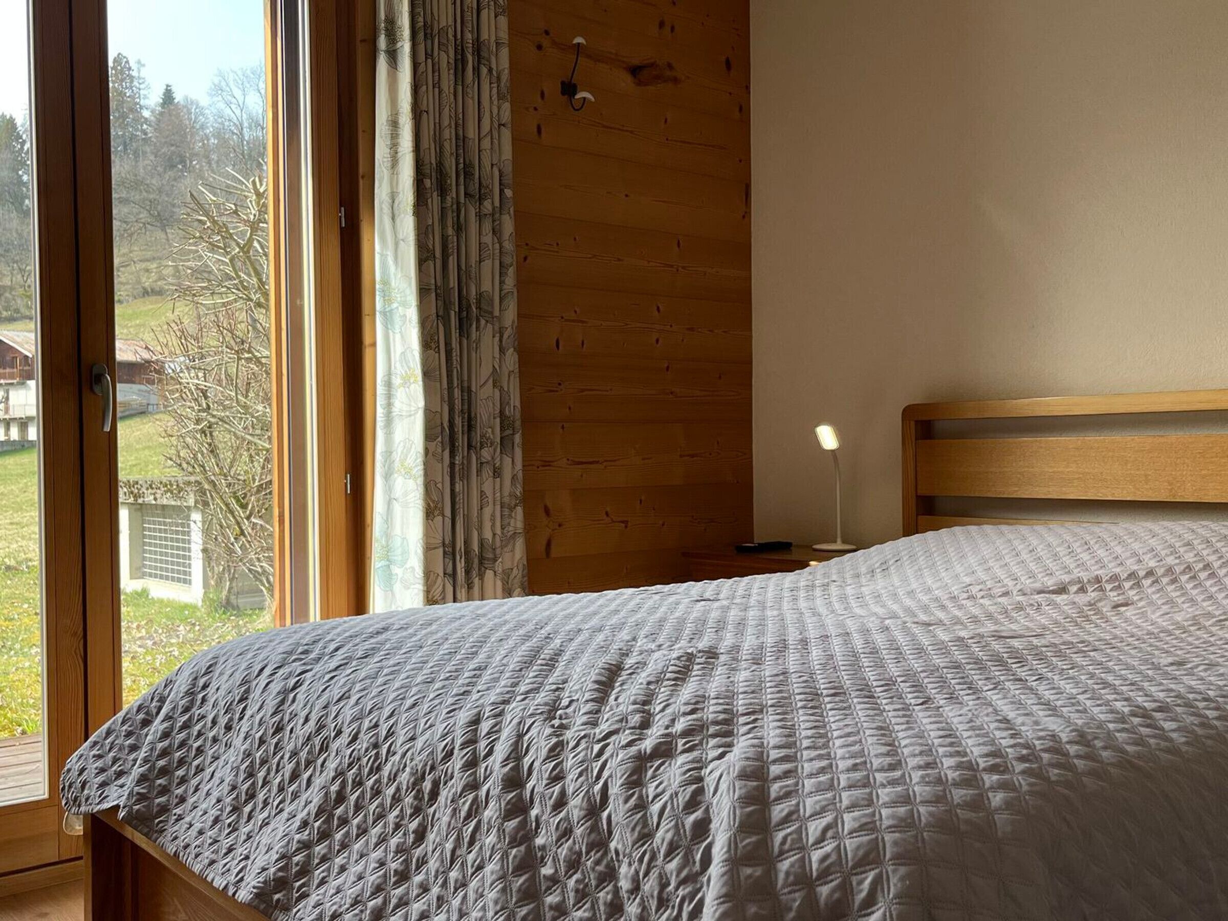 A bedroom with a large window, wooden headboard, and a quilted bedspread.