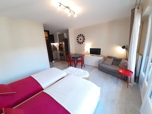 Una habitación con cama, sofá, televisor y zona de comedor con sillas y mesa.