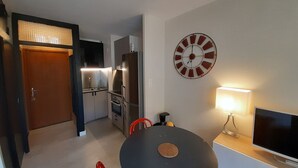 A compact kitchen with modern appliances, a dining area with a table and chairs, and a wall clock. - Renovated studio in the center for 2 people (Brides-les-Bains)