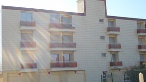 Un immeuble à plusieurs étages doté de balcons, d’un toit plat et d’une entrée fermée par un portail.