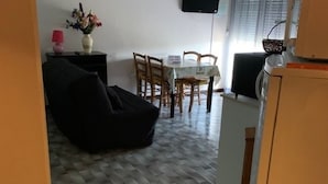 Une pièce comprenant un fauteuil en forme de sac de haricots noir, une table à manger avec des chaises, un petit meuble blanc et un téléviseur fixé au mur.