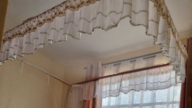 Ein Bett mit Baldachin, ein Fenster mit Vorhängen und Blick ins Freie.