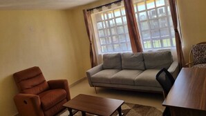 Ein Wohnzimmer mit einer Couch, einem Sessel, einem Tisch und einem Fenster mit Vorhängen.